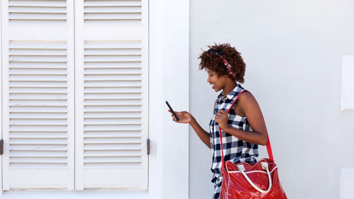 smiling african woman walking with cellphone and