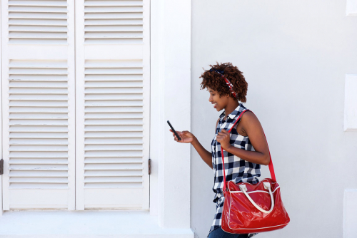smiling african woman walking with cellphone and